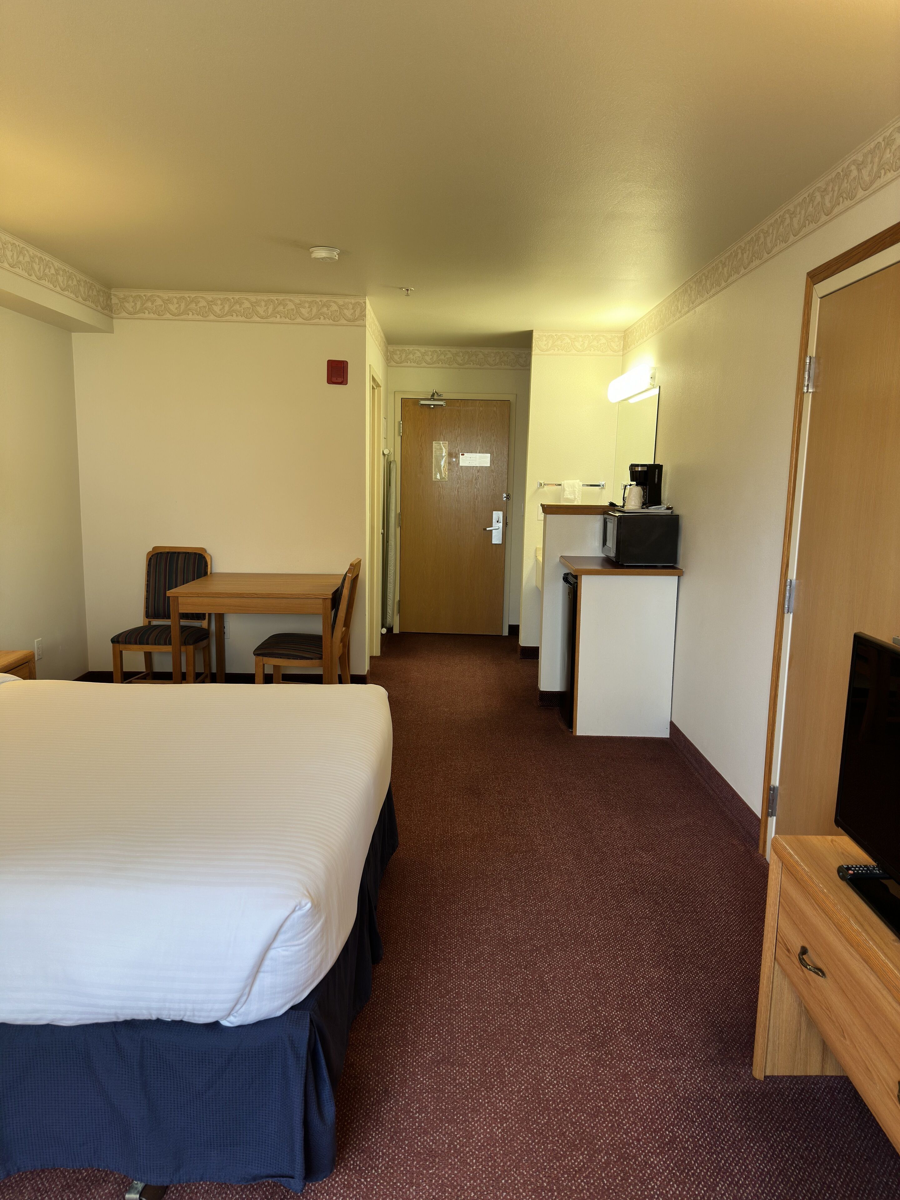A hotel room with a bed, a desk, a chair, a television, and a microwave.