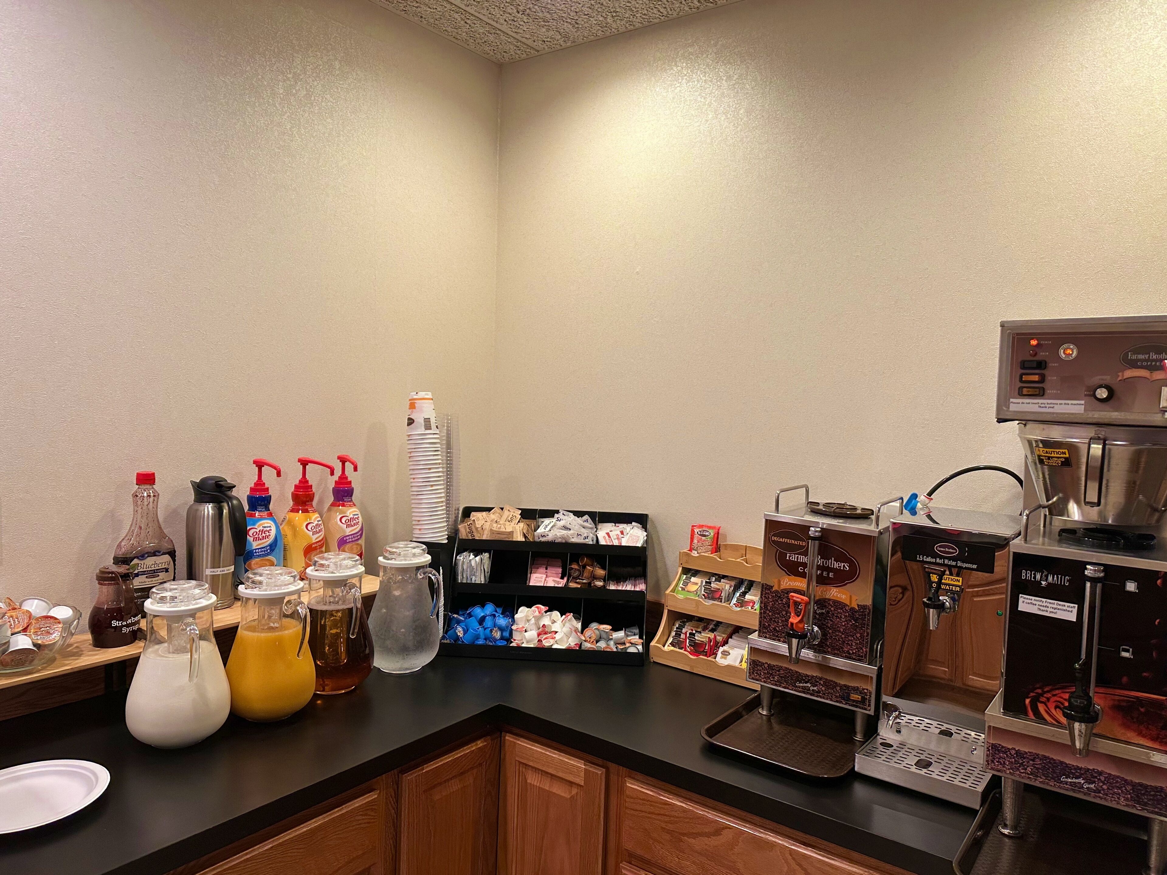 A breakfast bar with coffee machines, condiment dispensers, and a variety of beverages.