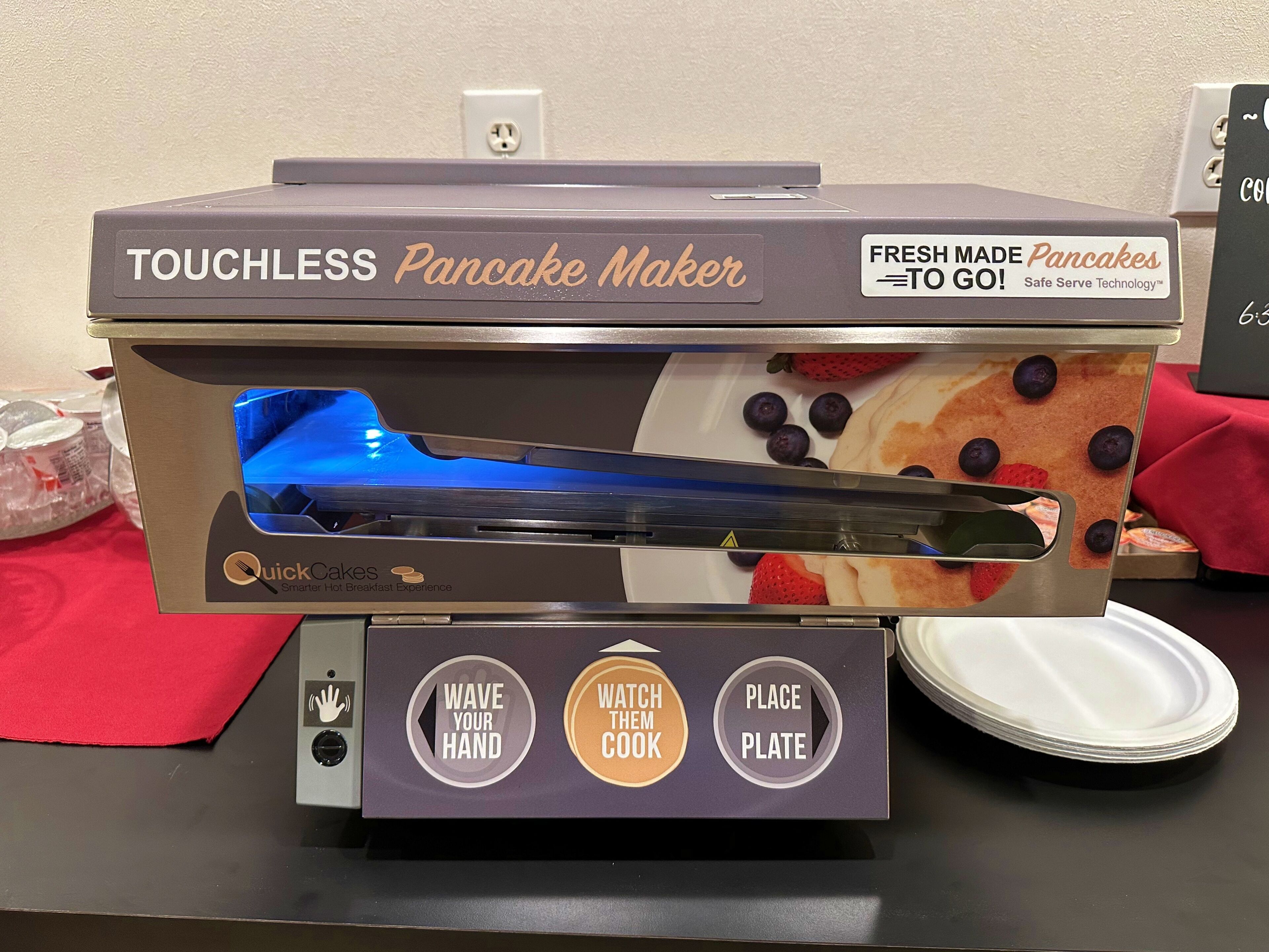 A touchless pancake maker with instructions to wave your hand, watch the cook, and place the plate.