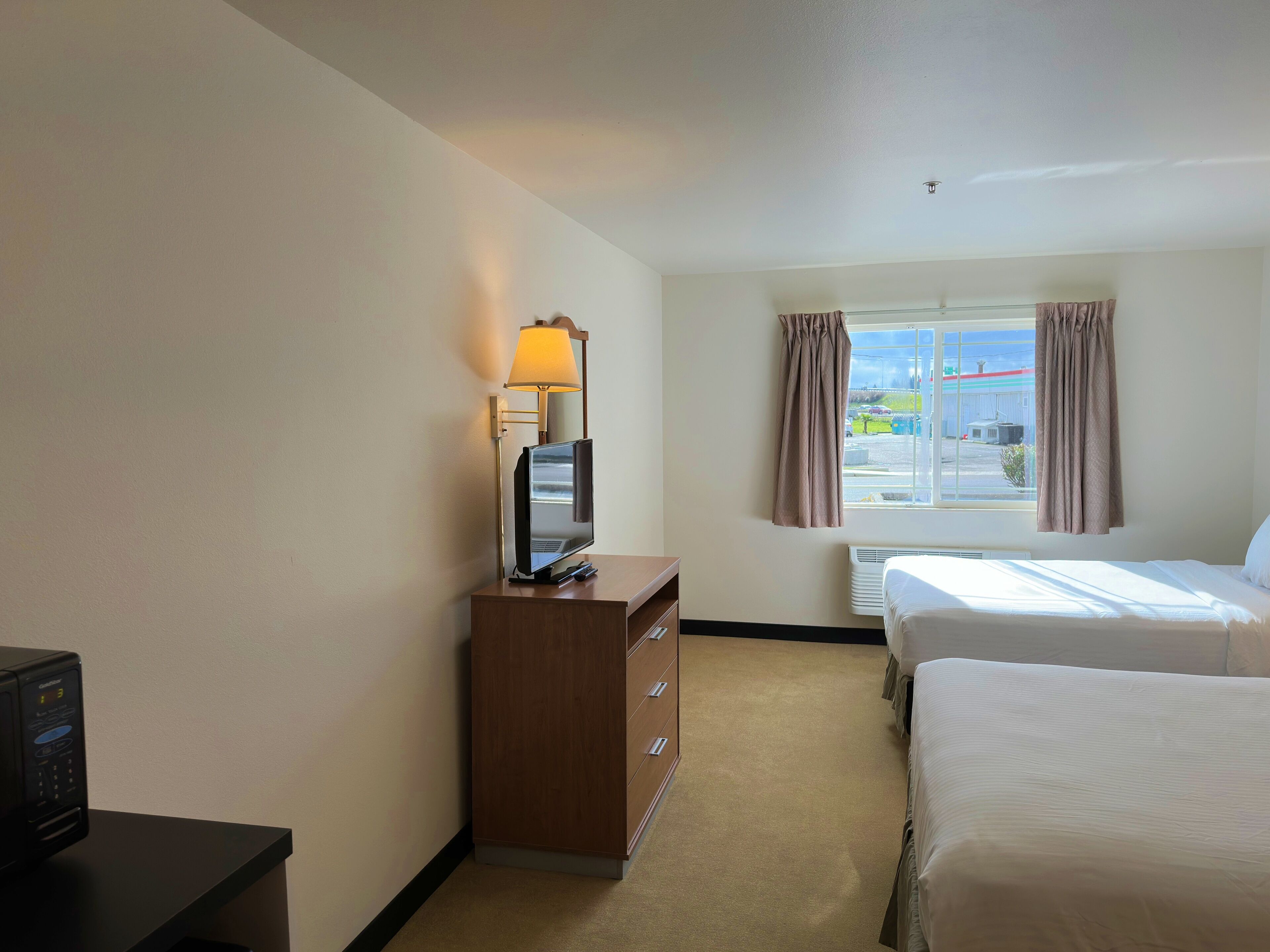 Une chambre d’hôtel avec un lit, un bureau avec une lampe, une télévision et une fenêtre avec des rideaux.