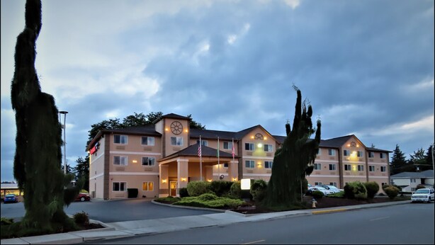 A multi-story hotel with a central entrance, flagpoles, and a parking lot. - Peppermill Empress Inn (Centralia)
