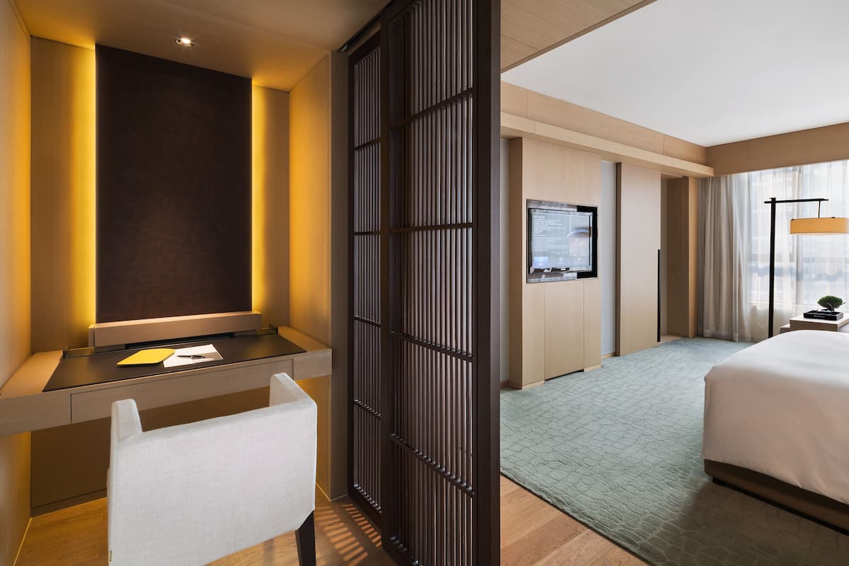 Een moderne hotelkamer met een groot bed, een bureau met stoel, een televisie en stadszicht door grote ramen.