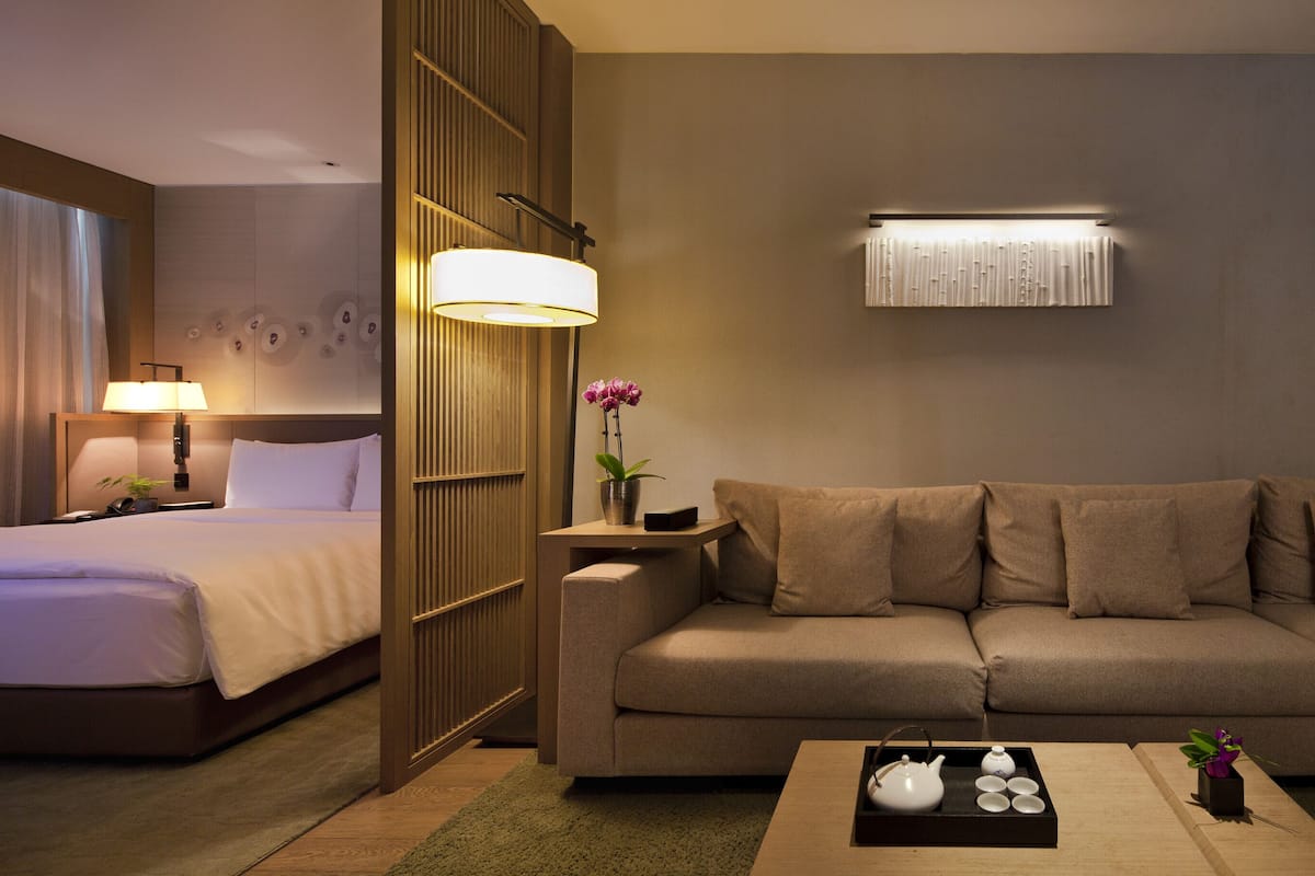 Een hotelkamer met een bed, een slaapbank, een bijzettafeltje met theeservies en een wandlamp.