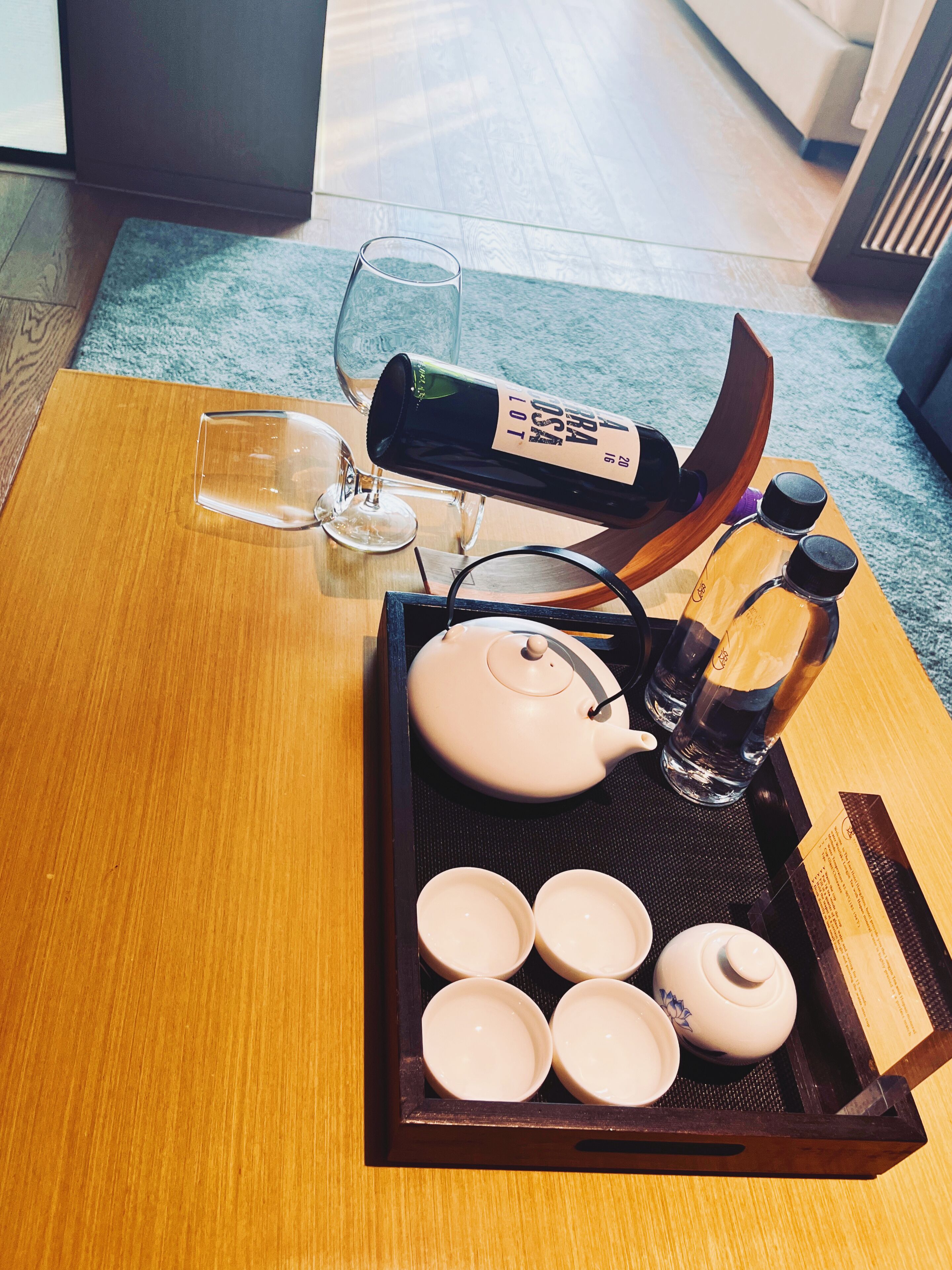 Ein Holztablett mit einem Teekessel, Teetassen, einem Glas und Flaschen auf einem Tisch.