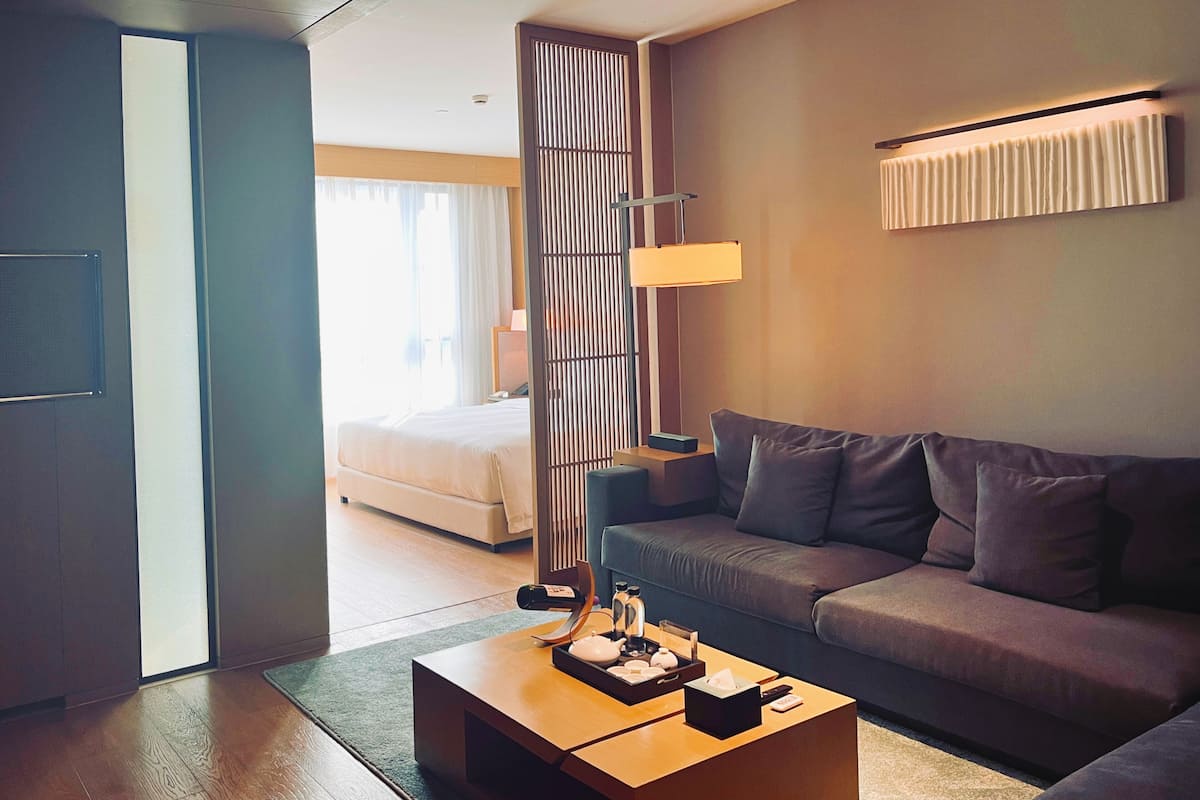 Een moderne hotelkamer met een houten salontafel, een grijze bank en een bed met witte lakens.