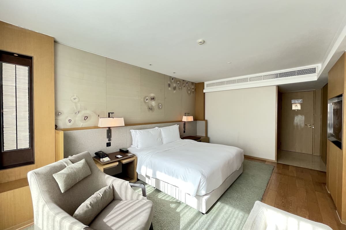 Een hotelkamer met een bed, twee nachtkastjes, een stoel, een bureau, een lamp, een wandventilatoren en een deur.