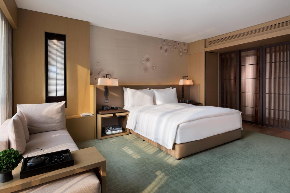 Een moderne hotelkamer met een groot bed, nachtkastjes, een bank en uitzicht.