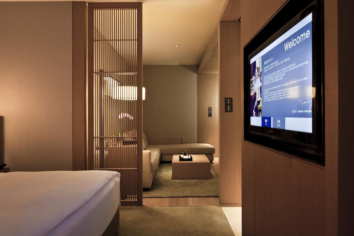 Een moderne hotelkamer met een bed, een bedlampje, een televisie en een schuifdeur naar een zithoek.