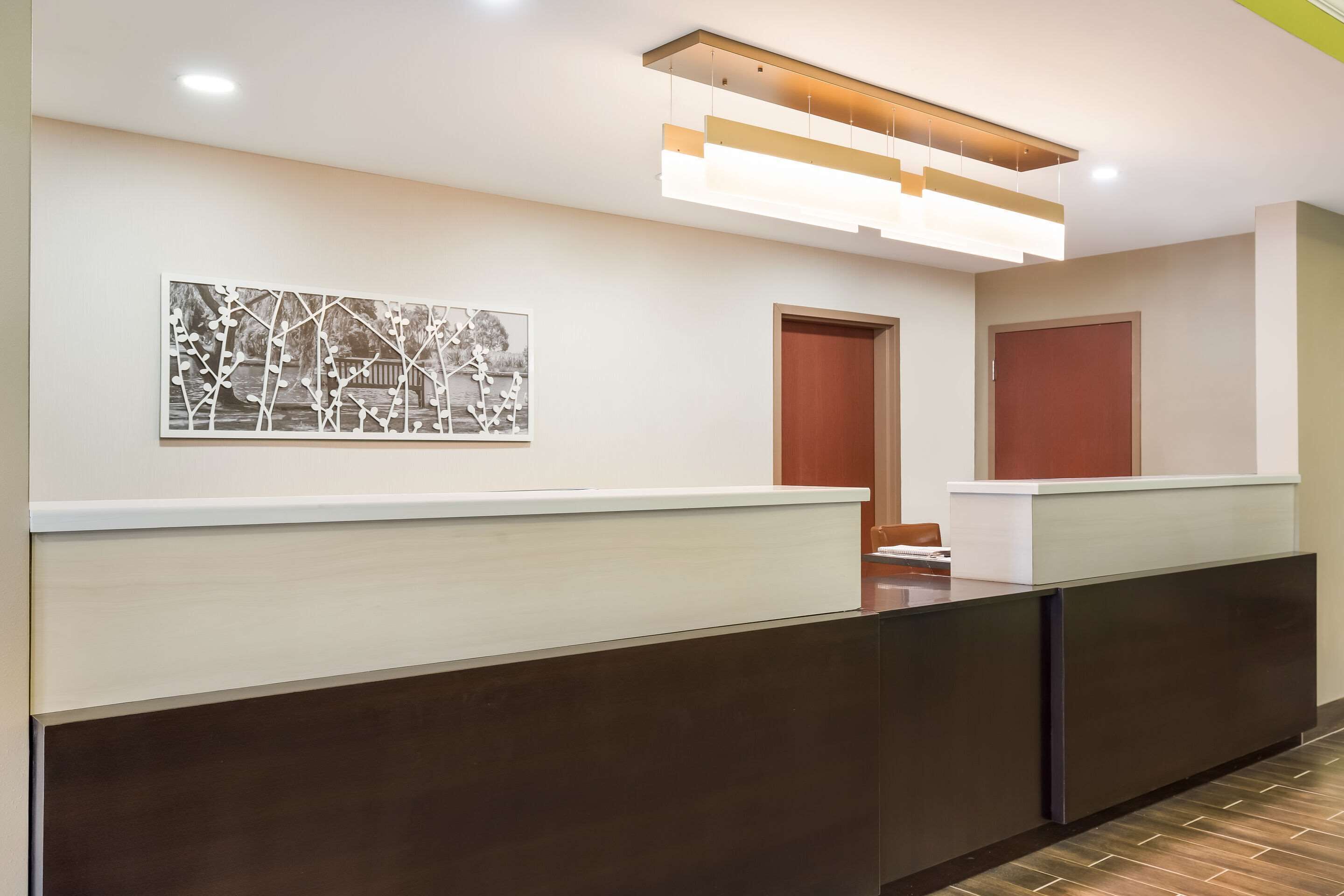 A reception area with a modern design, featuring a reception desk, a wall-mounted artwork, and a ceiling light fixture.