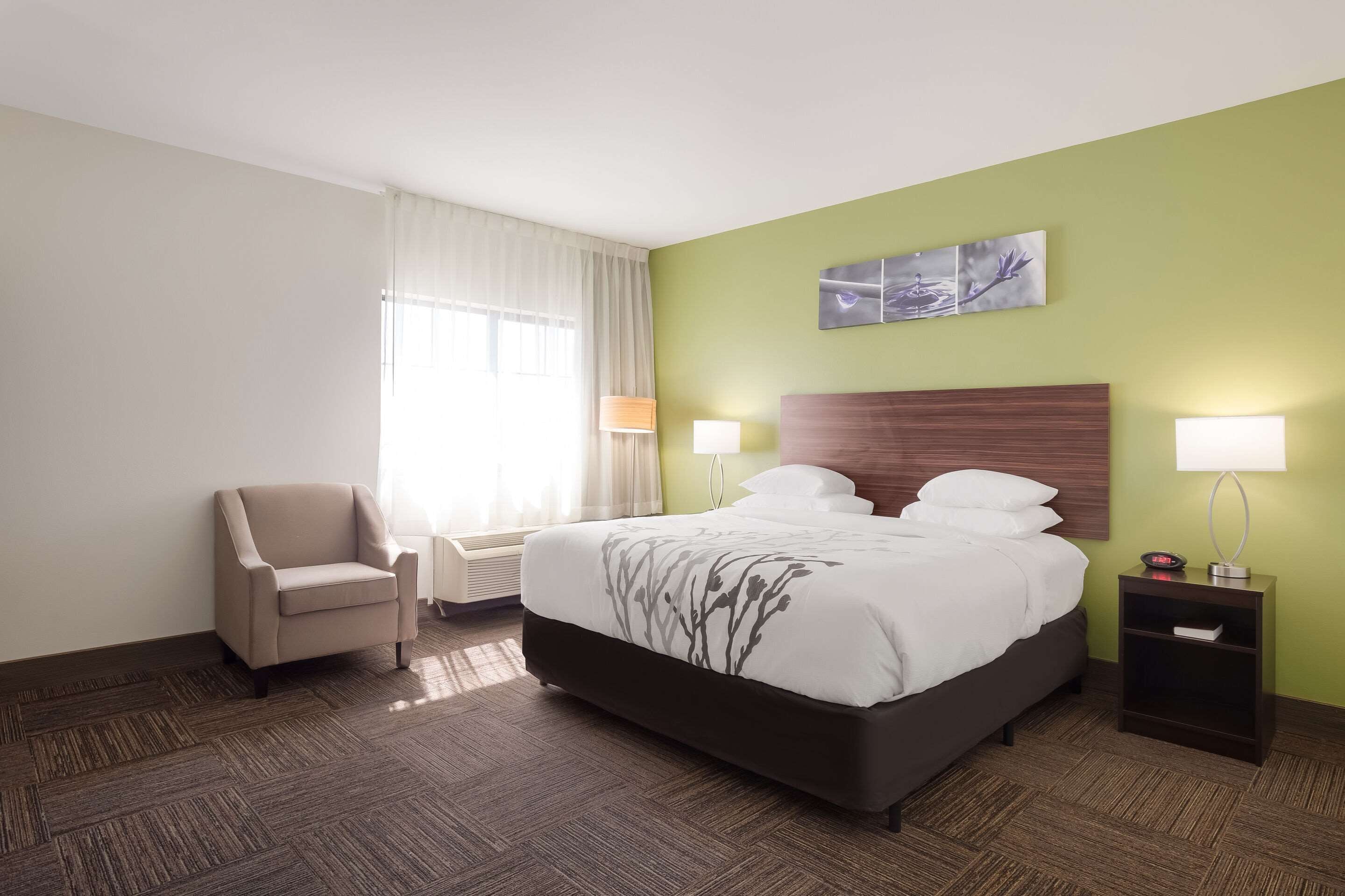Une chambre d’hôtel avec un lit, une chaise, une table de chevet et une lampe fixée au mur.