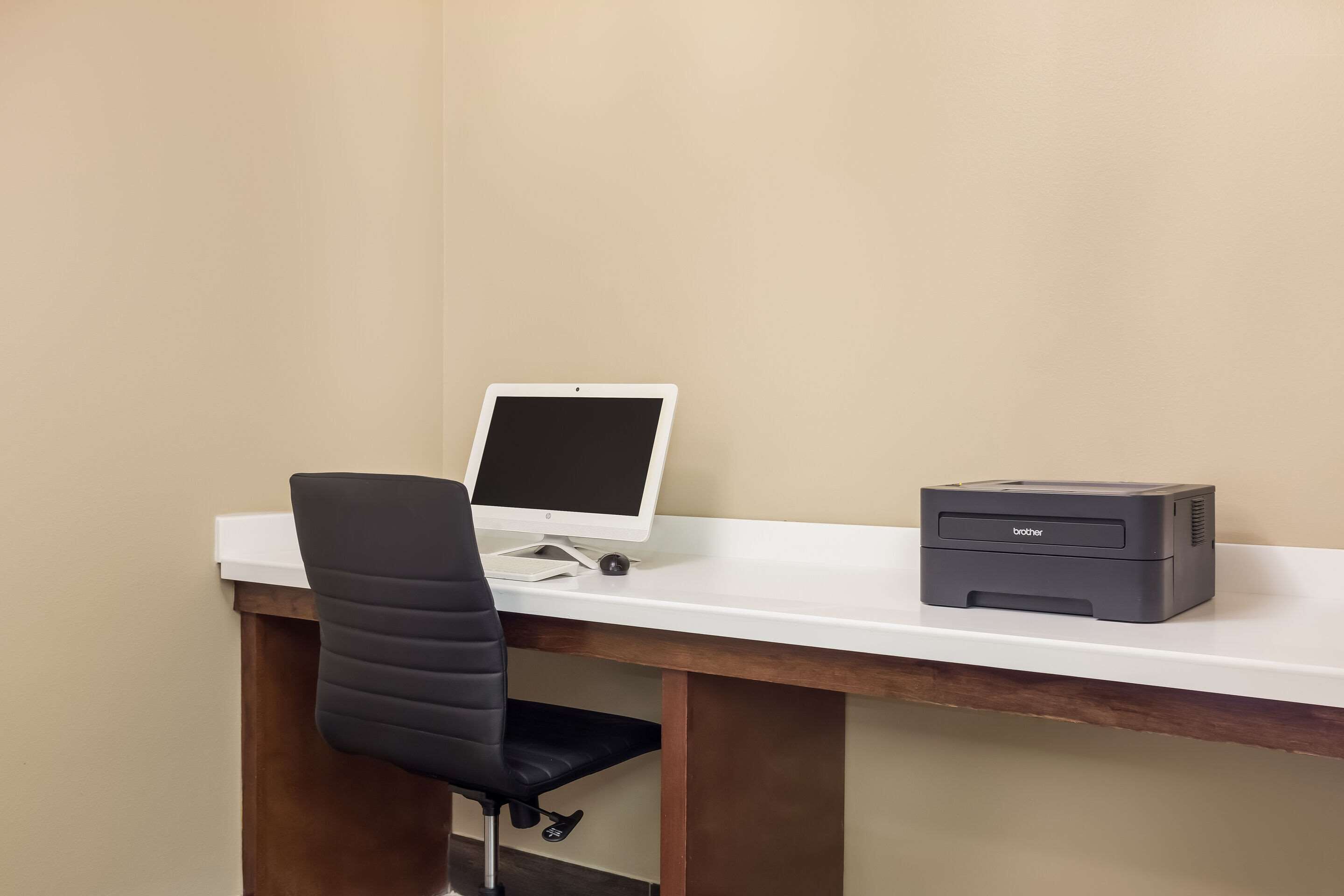 A desk with a computer monitor, a printer, and a black office chair.
