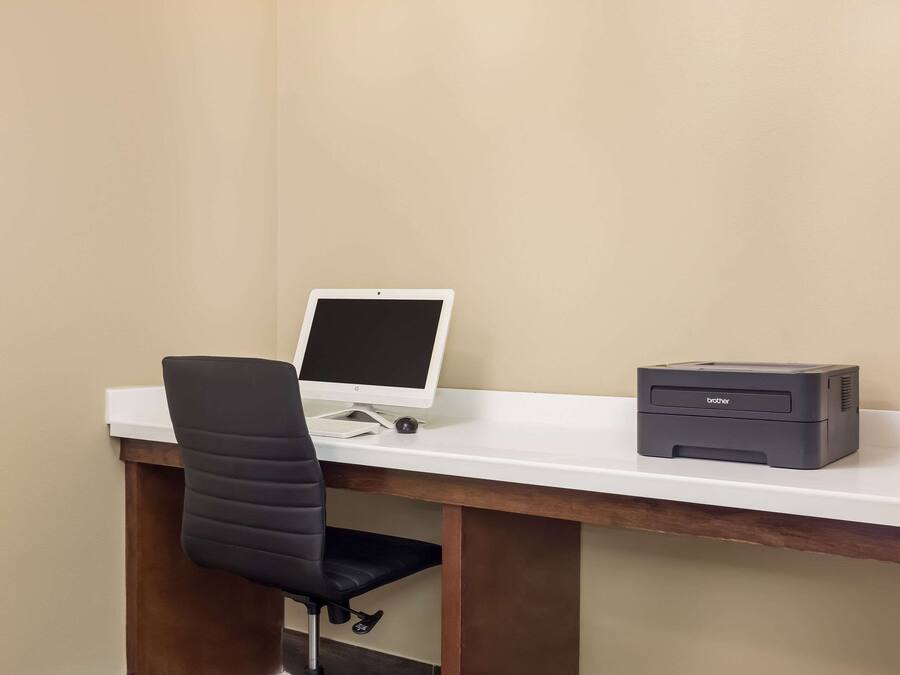 A desk with a computer monitor, a printer, and a black office chair.
