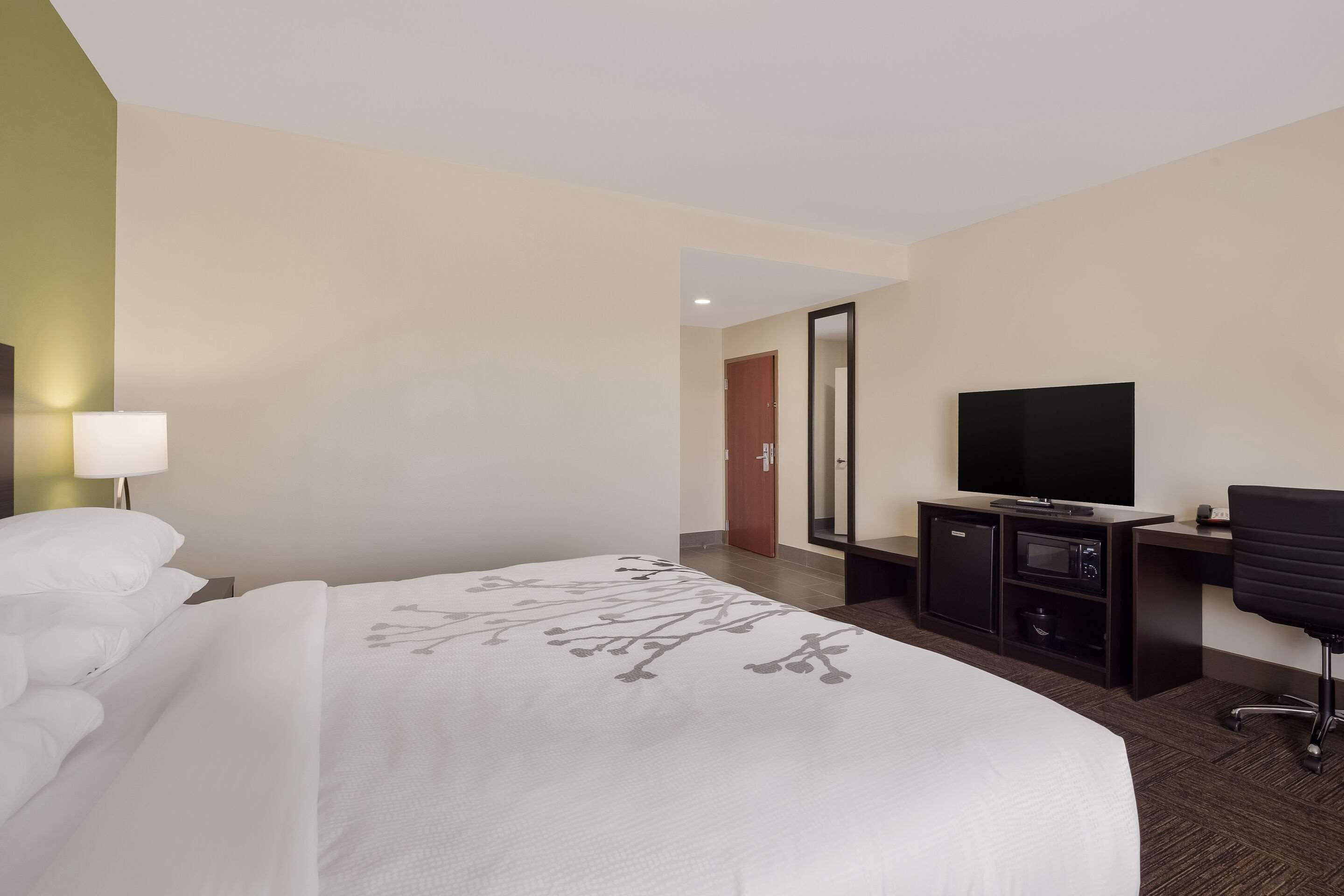 A hotel room with a bed, a desk with a television, a microwave, and a chair.