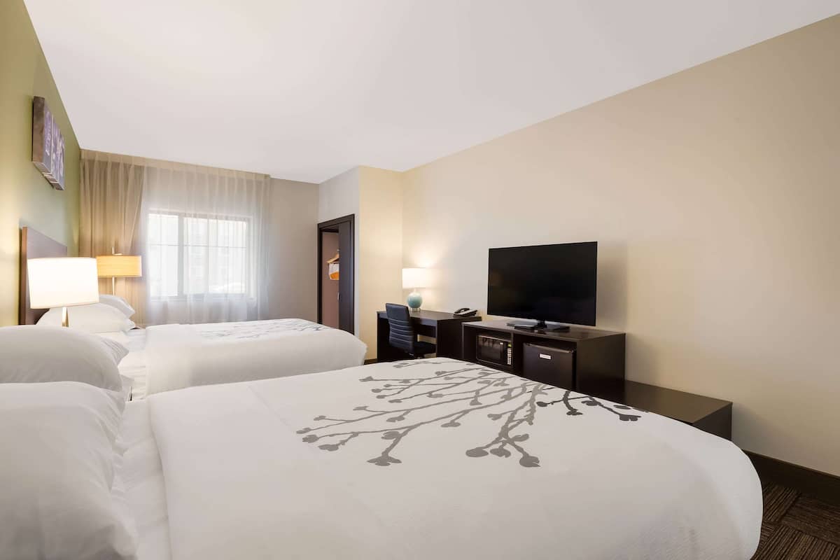 Habitación de hotel con dos camas, un escritorio con televisor y una lámpara.