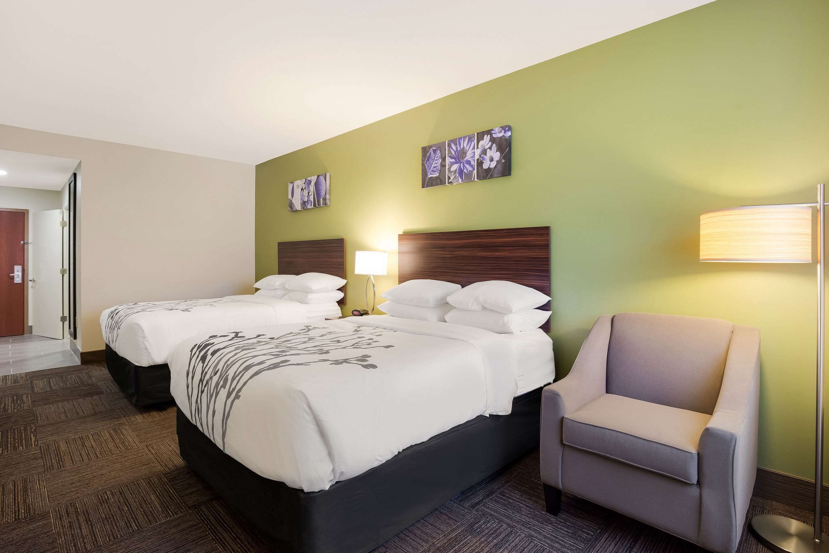 A hotel room with two beds, a chair, and artwork on the wall.
