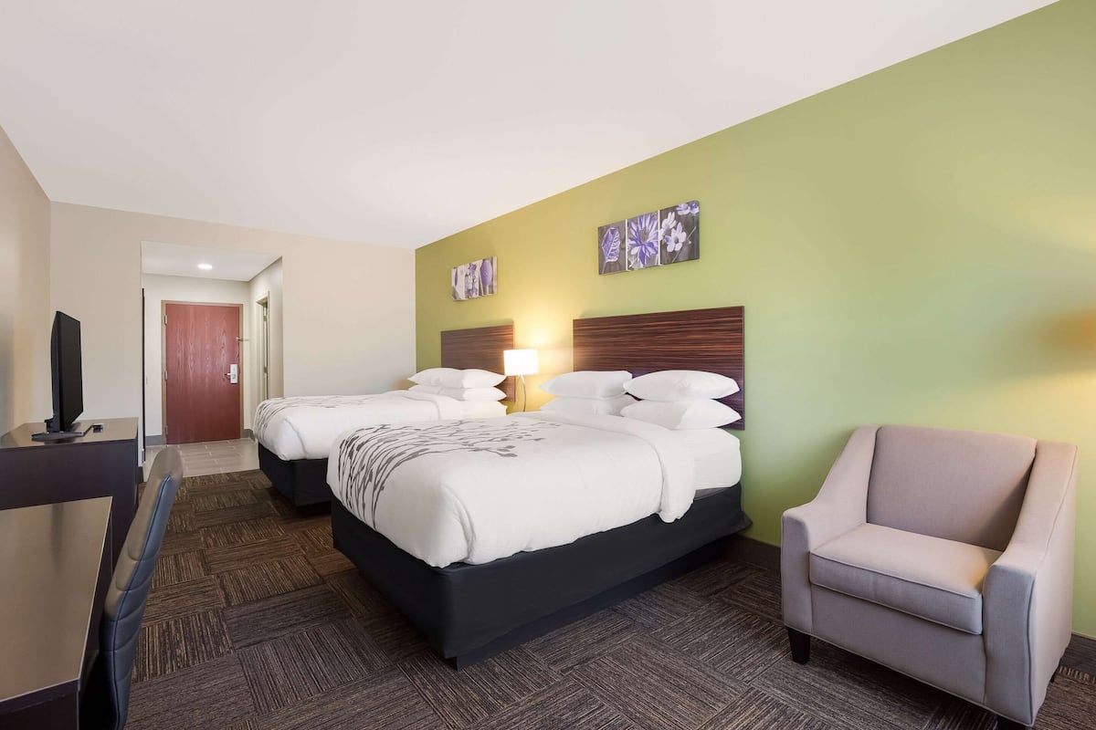Una habitación de hotel con dos camas, un escritorio, una silla y obras de arte en la pared.