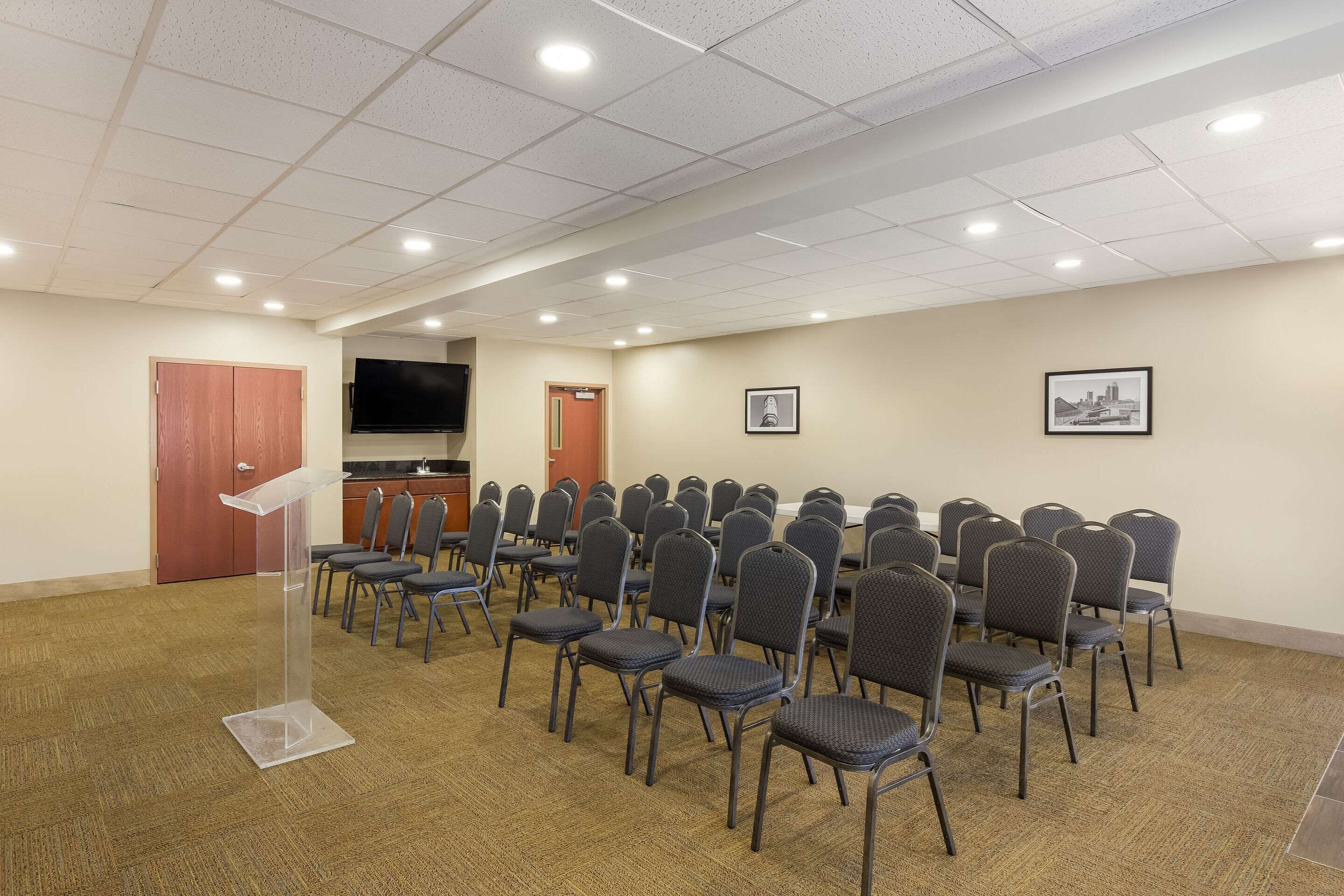 Une salle de conférence équipée d’un pupitre, de rangées de chaises, d’un téléviseur à écran plat et de tableaux encadrés aux murs.