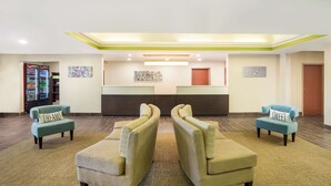 A lobby with a reception desk, two armchairs with pillows, a vending machine, and artwork on the walls. - Sleep Inn & Suites North Mobile Saraland (Saraland)
