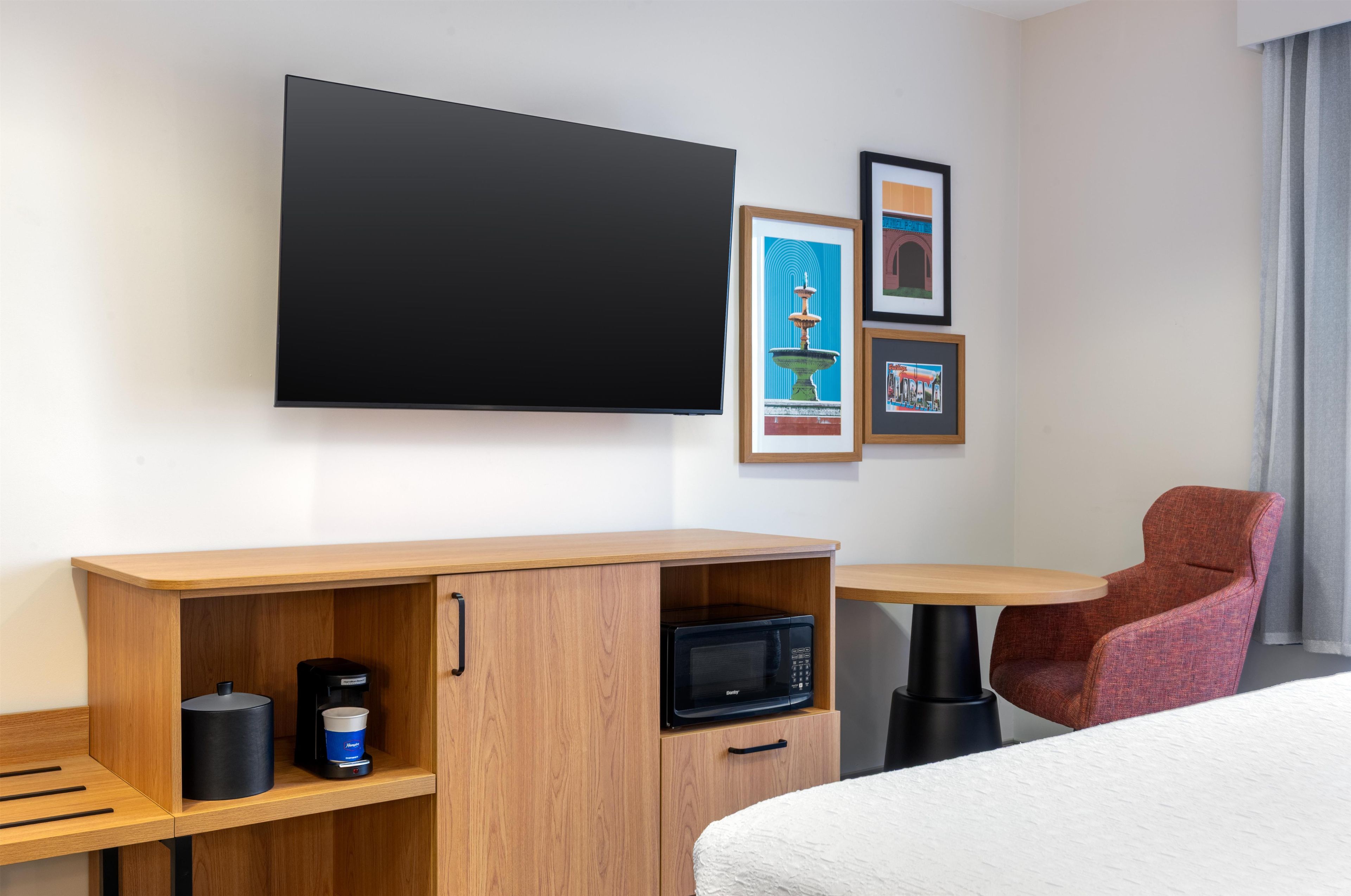 Habitació d'hotel amb televisió de pantalla plana penjada a la paret, escriptori de fusta amb una cafetera, microones i una poltrona vermella.