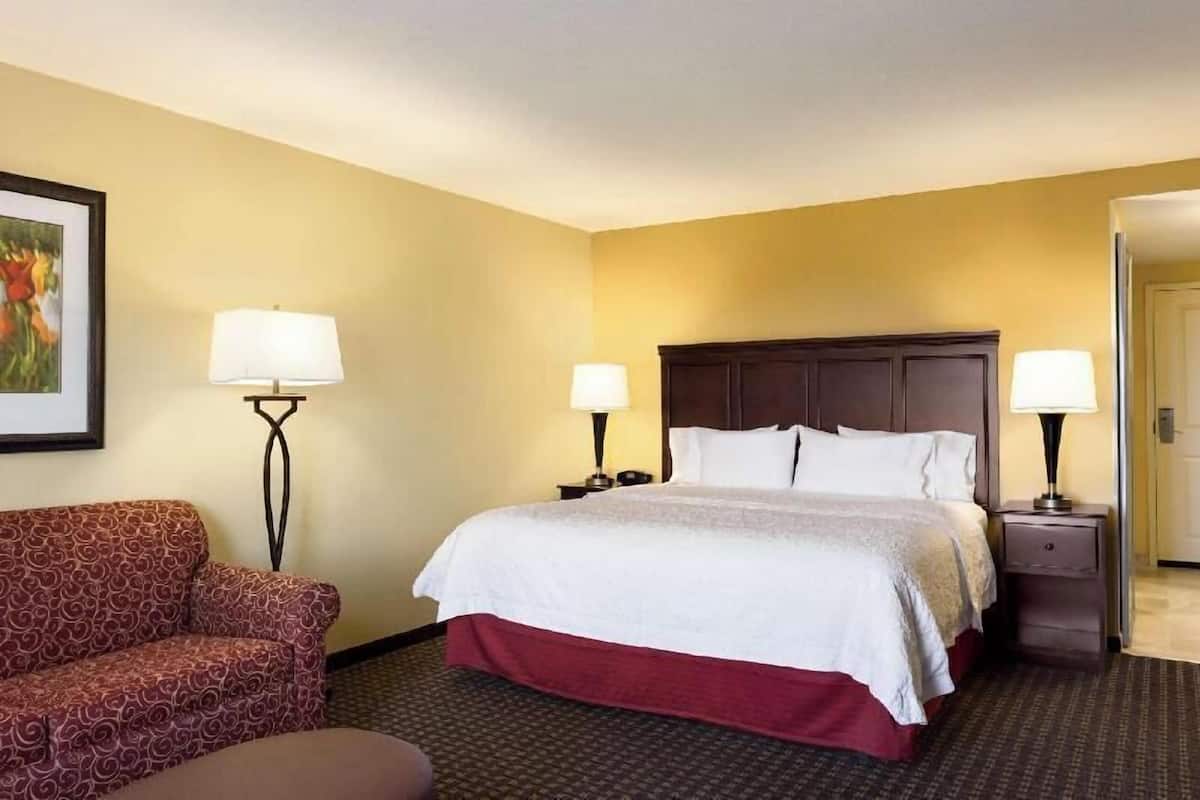 A hotel room with a bed, two bedside tables with lamps, a sofa, and a framed picture on the wall.