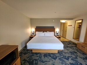 A hotel room with a large bed, bedside lamps, a wooden nightstand, a mirror, and a carpeted floor. - Hampton Inn & Suites Prattville (Prattville)