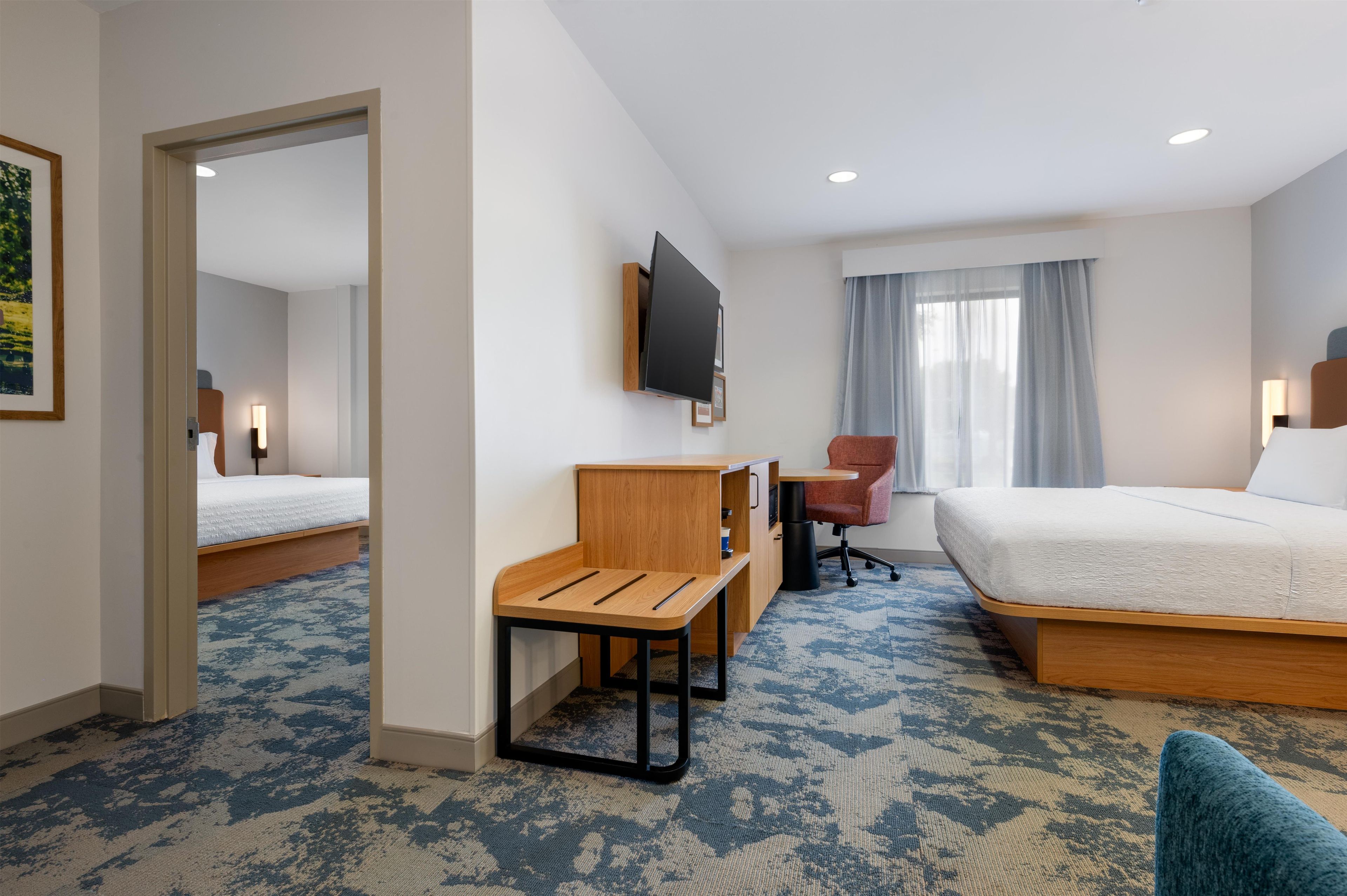 Habitación de hotel con cama, escritorio, silla, televisión y ventana con cortinas.