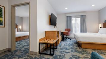 Habitación de hotel con cama, escritorio, silla, televisión y ventana con cortinas.