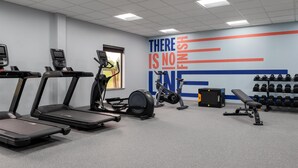 Une salle de sport équipée de tapis de course, de vélos elliptiques, d’un mur orné de citations motivantes et d’un porte-haltères.