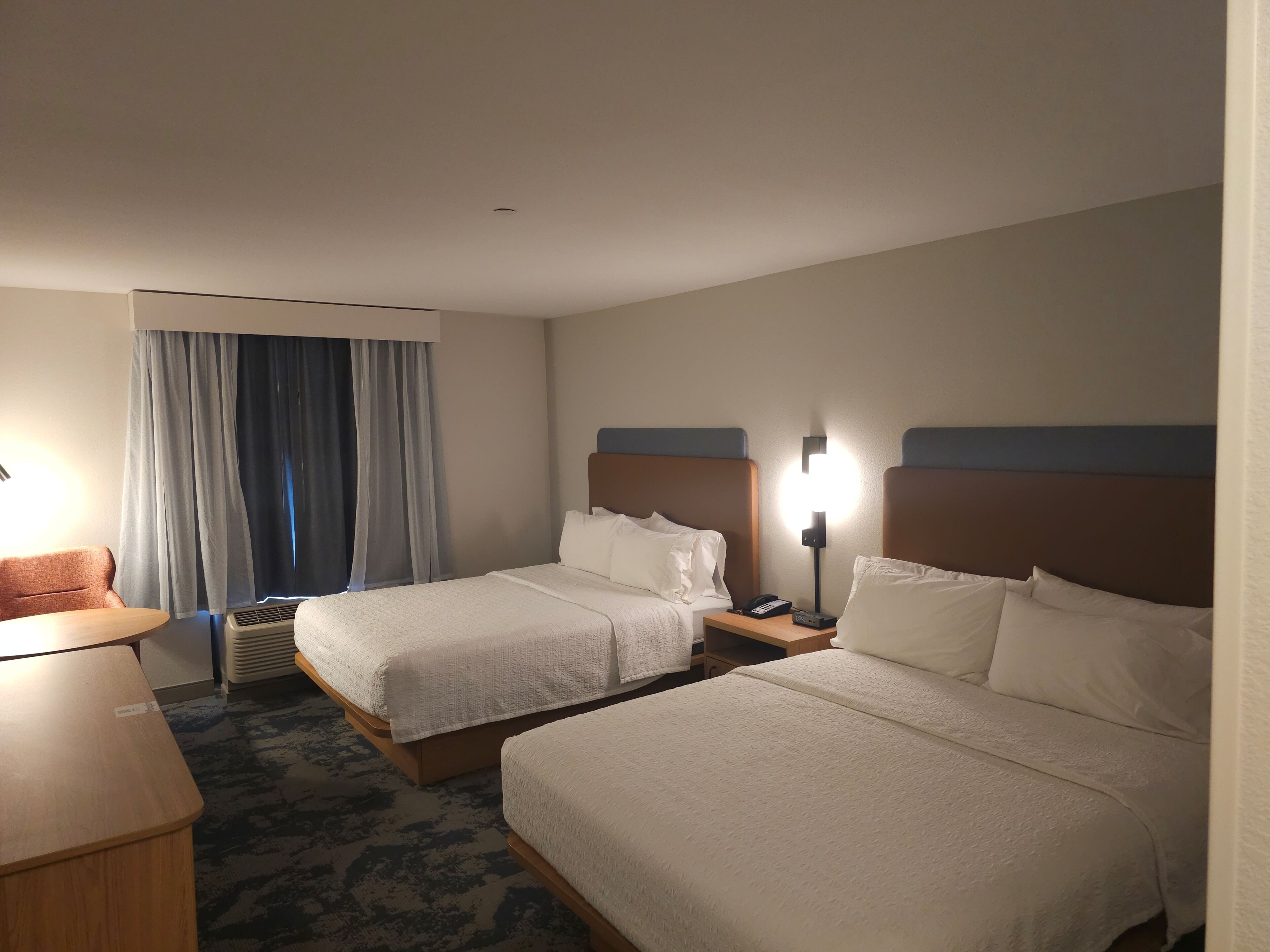 Een hotelkamer met twee bedden, een bureau, een stoel en een raam met gordijnen.
