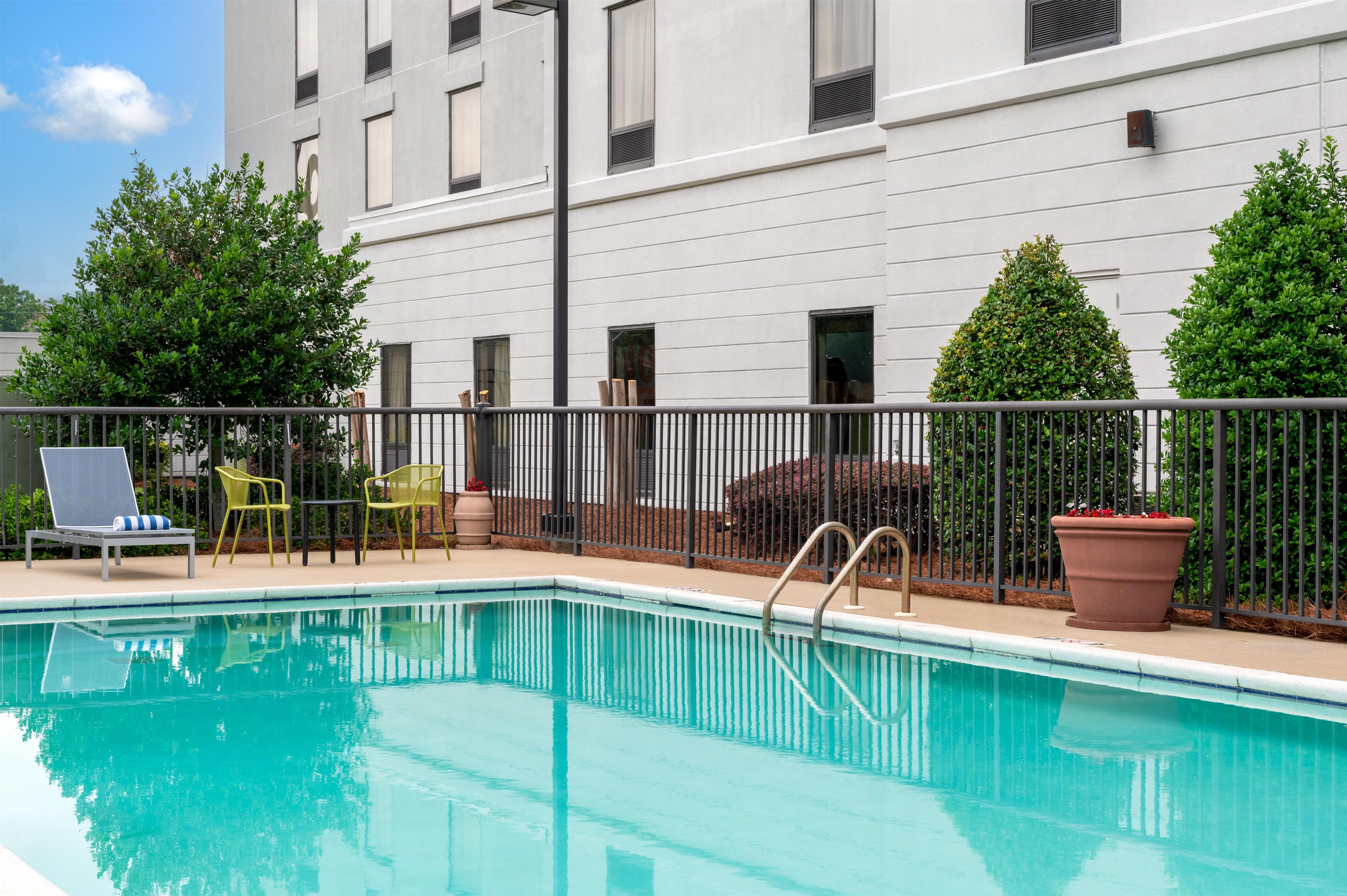 A swimming pool with a metal fence, chairs, and potted plants.