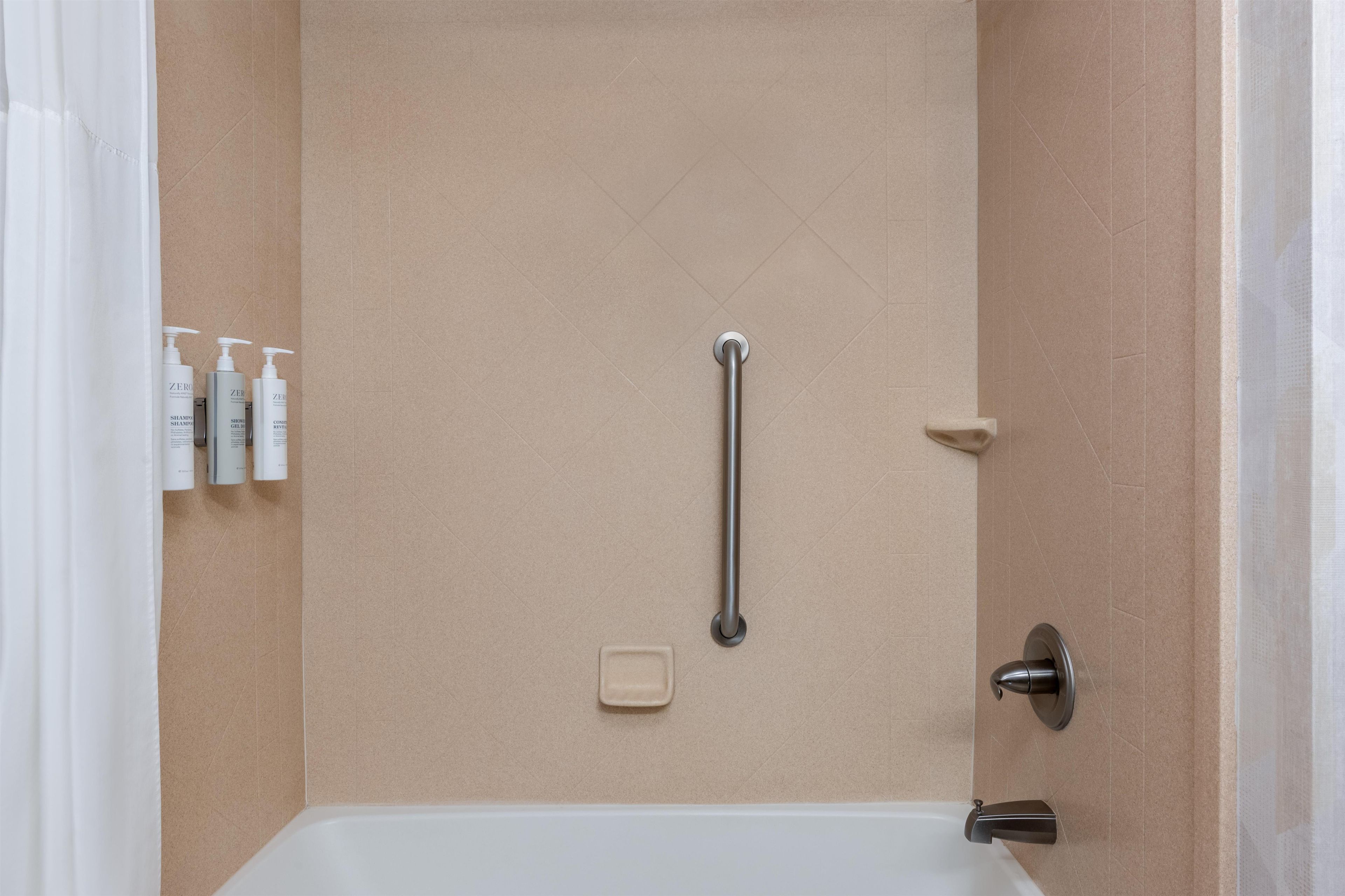 A bathroom with a bathtub, a handrail, and toiletries on the wall.