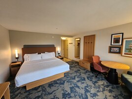 Habitación de hotel con una cama grande, mesitas de noche, un escritorio, una silla, un espejo y cuadros en la pared.