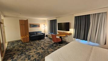 A hotel room with a bed, a sofa, a desk with a TV, a chair, and a painting on the wall.