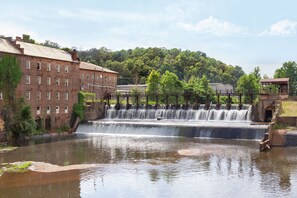 A historic building with a brick facade, a small waterfall, and a river in front. - Hampton Inn & Suites Prattville (Prattville)