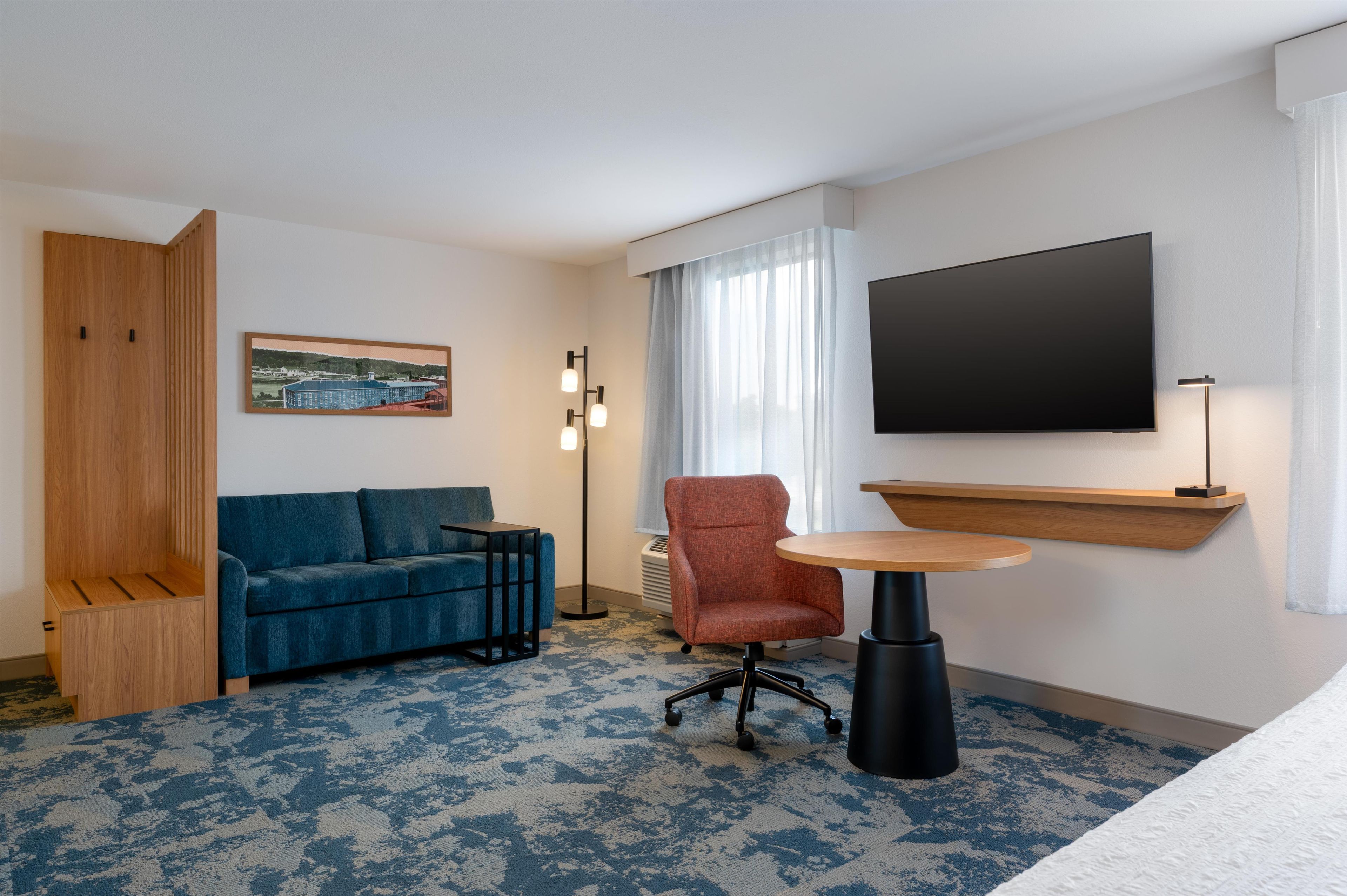 A hotel room with a sofa, armchair, small table, TV, and a painting on the wall.
