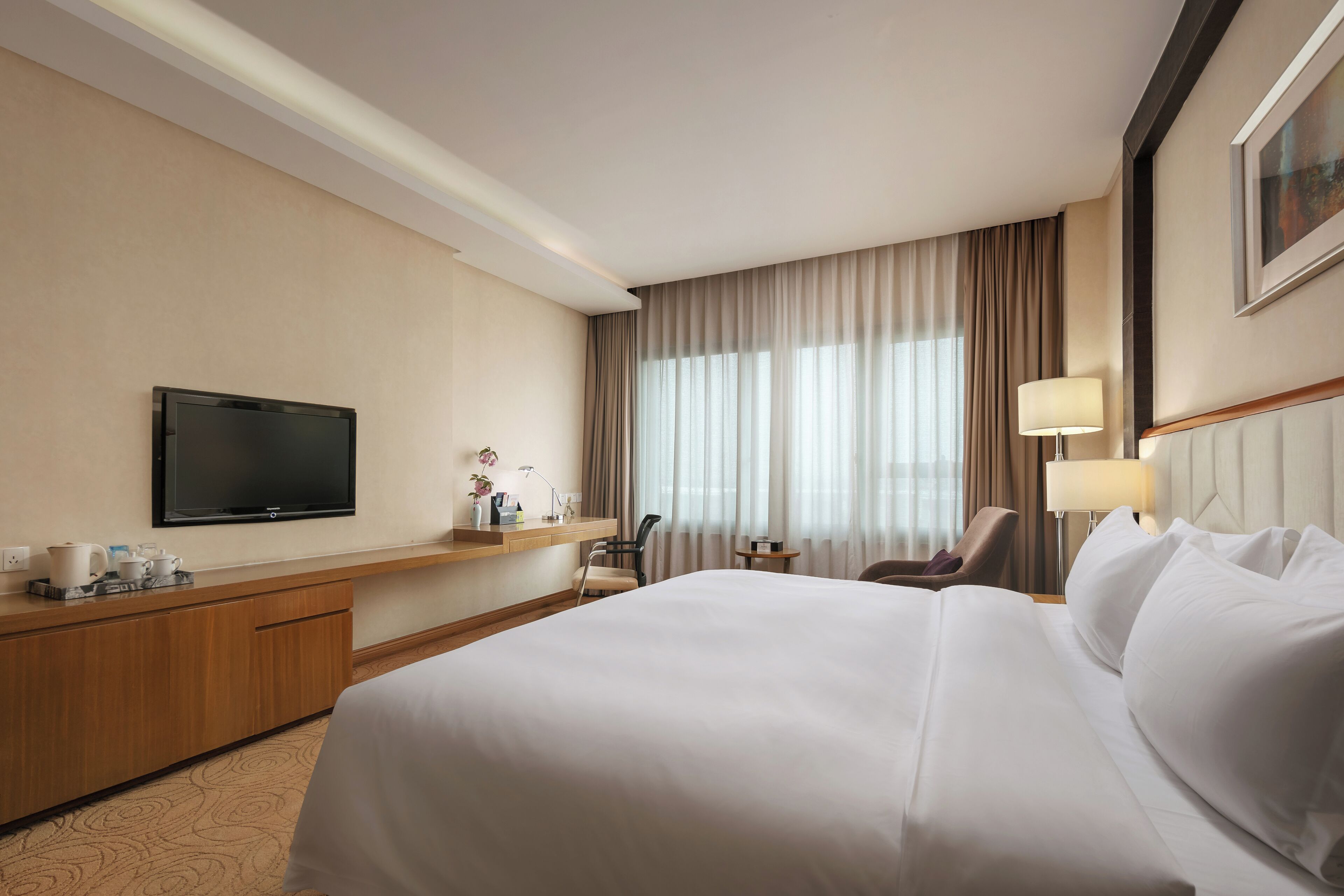 Ein Hotelzimmer mit einem großen Bett, einem Fernseher, einem Schreibtisch mit Lampe und einem Sessel.