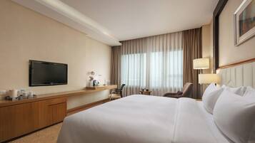 Ein Hotelzimmer mit einem großen Bett, einem Fernseher, einem Schreibtisch mit Lampe und einem Sessel.