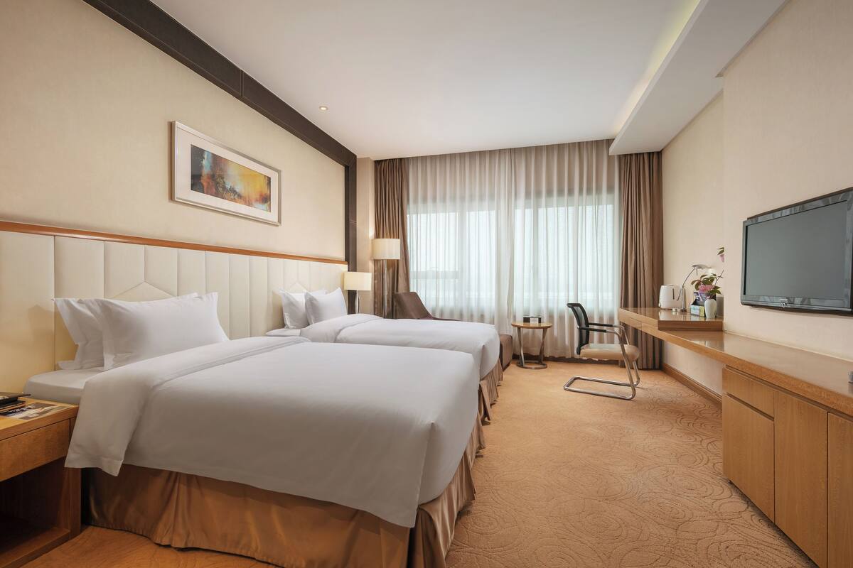 Hotelkamer met twee bedden, een bureau, een stoel, een televisie en een schilderij aan de muur.