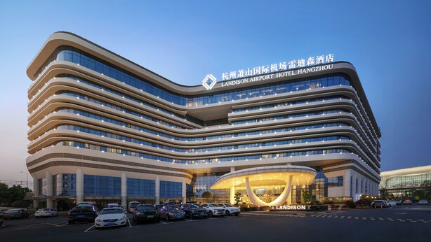 A modern hotel with a curved facade, multiple floors, and a prominent entrance with illuminated signage. - Landison Airport Hotel HangZhou (Hangzhou)