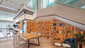 A modern indoor space with a wooden table, white chairs, a sofa, and a bean bag chair. There are bookshelves with books and decorative items. - Landison Airport Hotel HangZhou (Hangzhou)