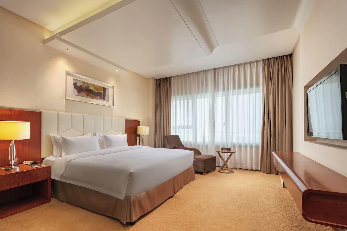 Een hotelkamer met een groot bed, een bureau met lamp, een stoel, een televisie en een schilderij aan de muur.