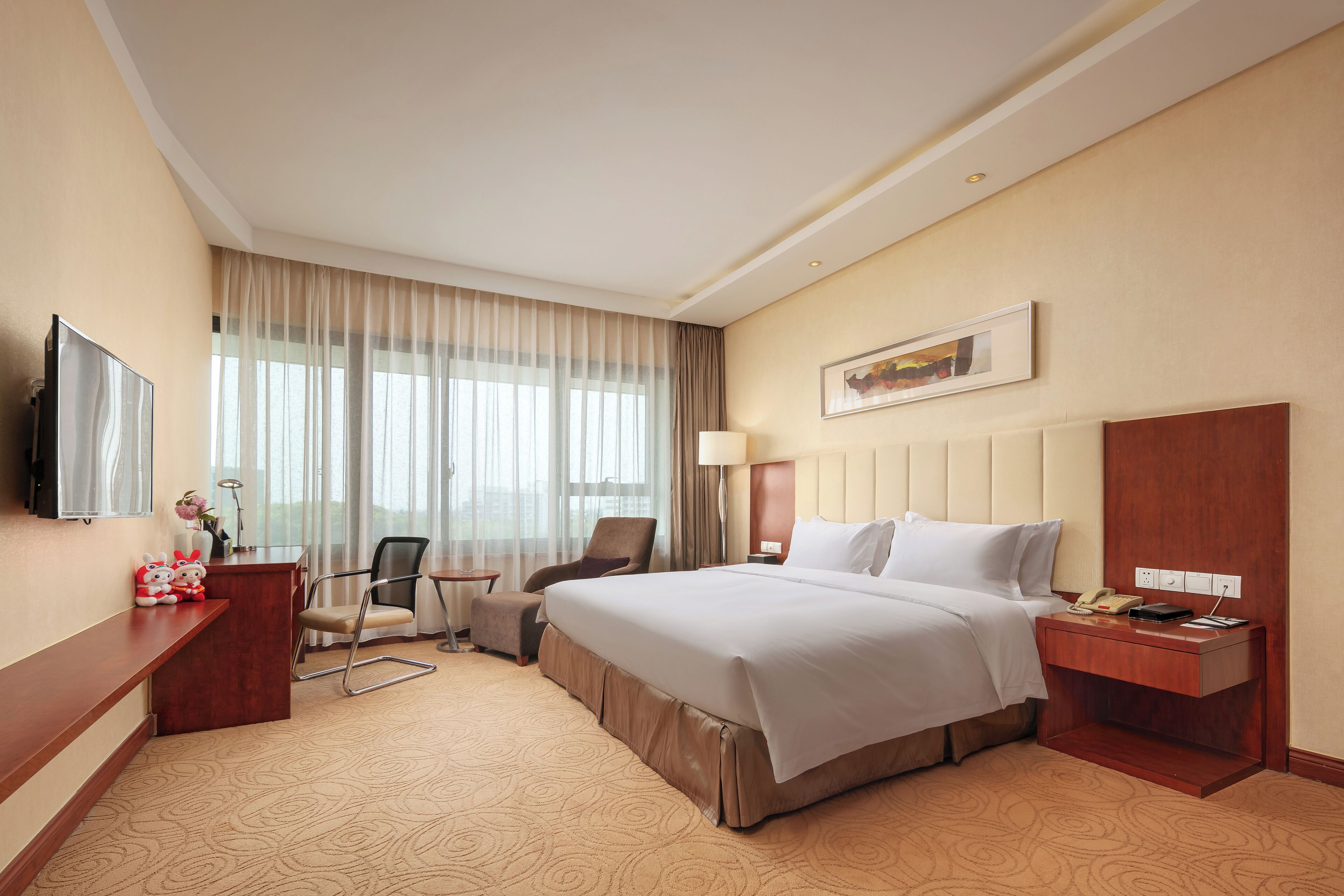 Una habitación de hotel con una cama grande, un escritorio, una silla, un televisor y una ventana con cortinas.