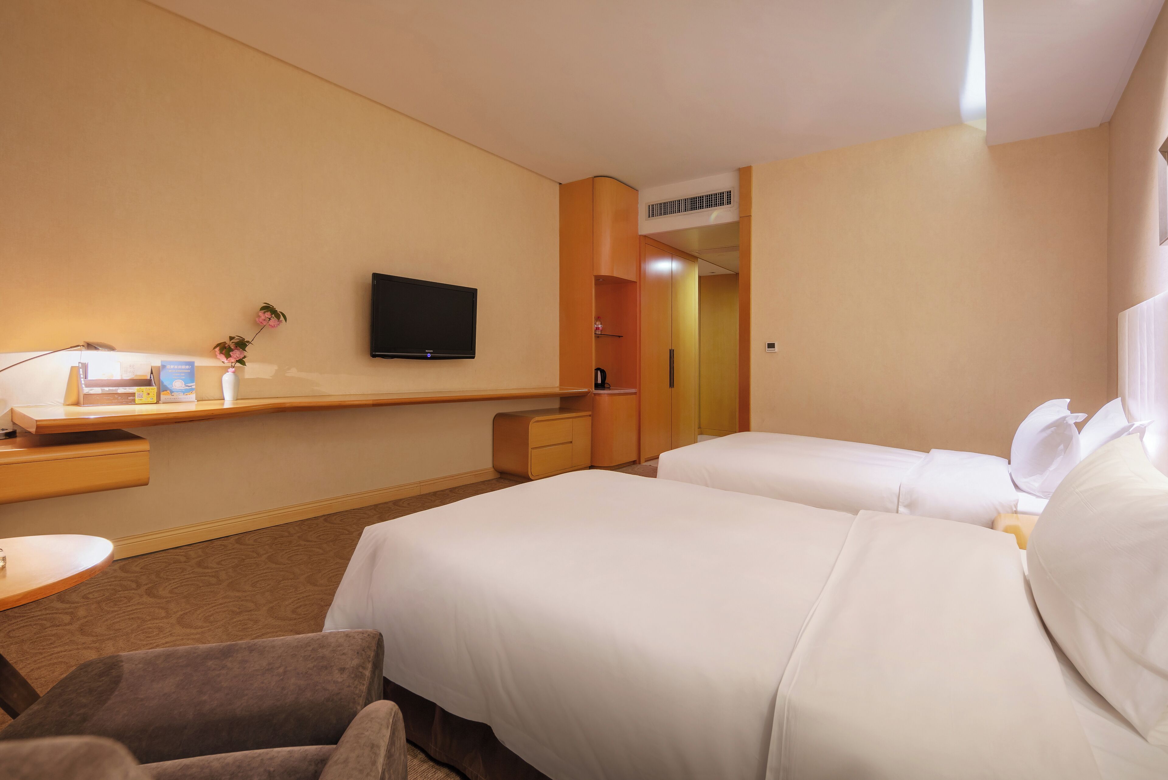 A hotel room with two beds, a TV, a desk with a lamp, and a small plant.
