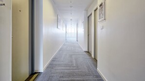 Un pasillo largo y estrecho con suelo alfombrado, paredes blancas y puertas a ambos lados.