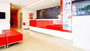 Un área de recepción moderna con una decoración en rojo y blanco, una recepción y un cartel que dice 'SHOP'.