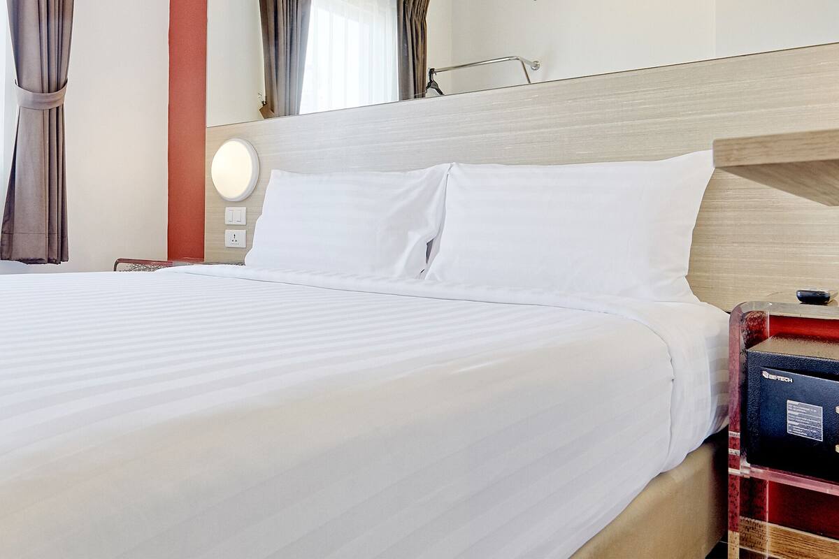 A hotel room with a large bed, a bedside table with a lamp, a mirror, and curtains on the windows.