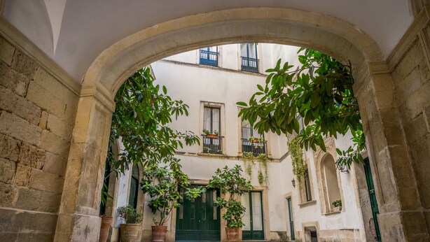 An arched courtyard with stone walls, potted plants, and a green door. - B&B Palazzo Bernardini Suite (Lecce)