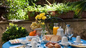 A table set with breakfast items including bread, pastries, fruit, and beverages, with a garden view in the background. - B&B Palazzo Bernardini Suite (Lecce)