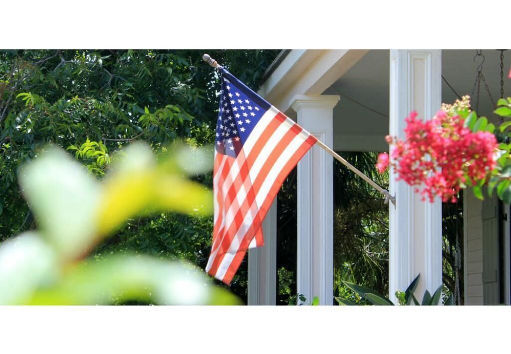 An American flag on a flagpole in front of a house with a porch.