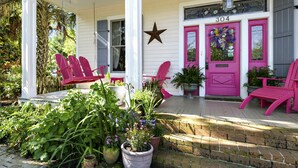 A porch with pink chairs, potted plants, and a star decoration. - Carroll House Cottages (Bay St Louis)